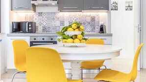 A modern kitchen with a white dining table, yellow chairs, and a fruit bowl on the table. - GuestHost - Vomero Deluxe Paris with terrace (Napoli)