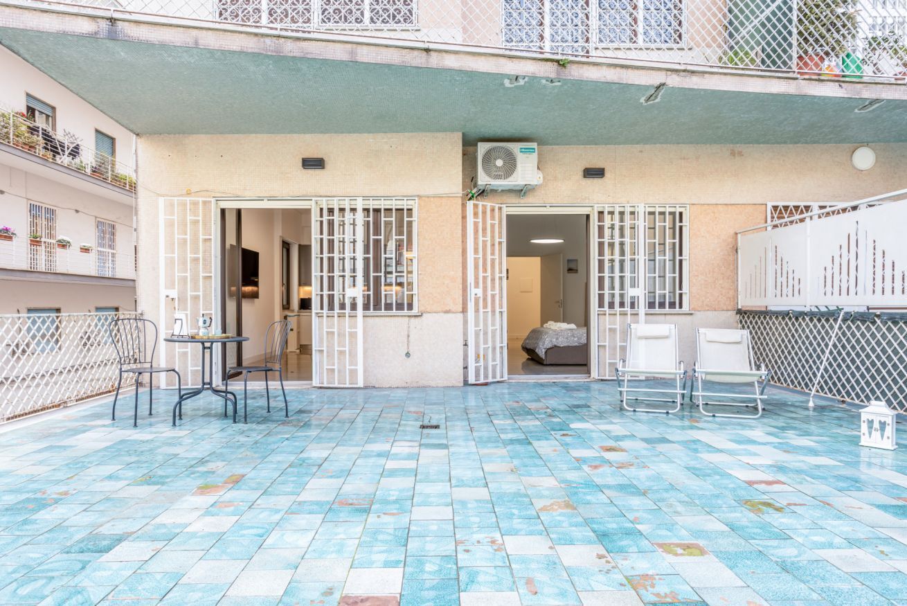 A courtyard with a tiled floor, a table with chairs, and a bed in the background.