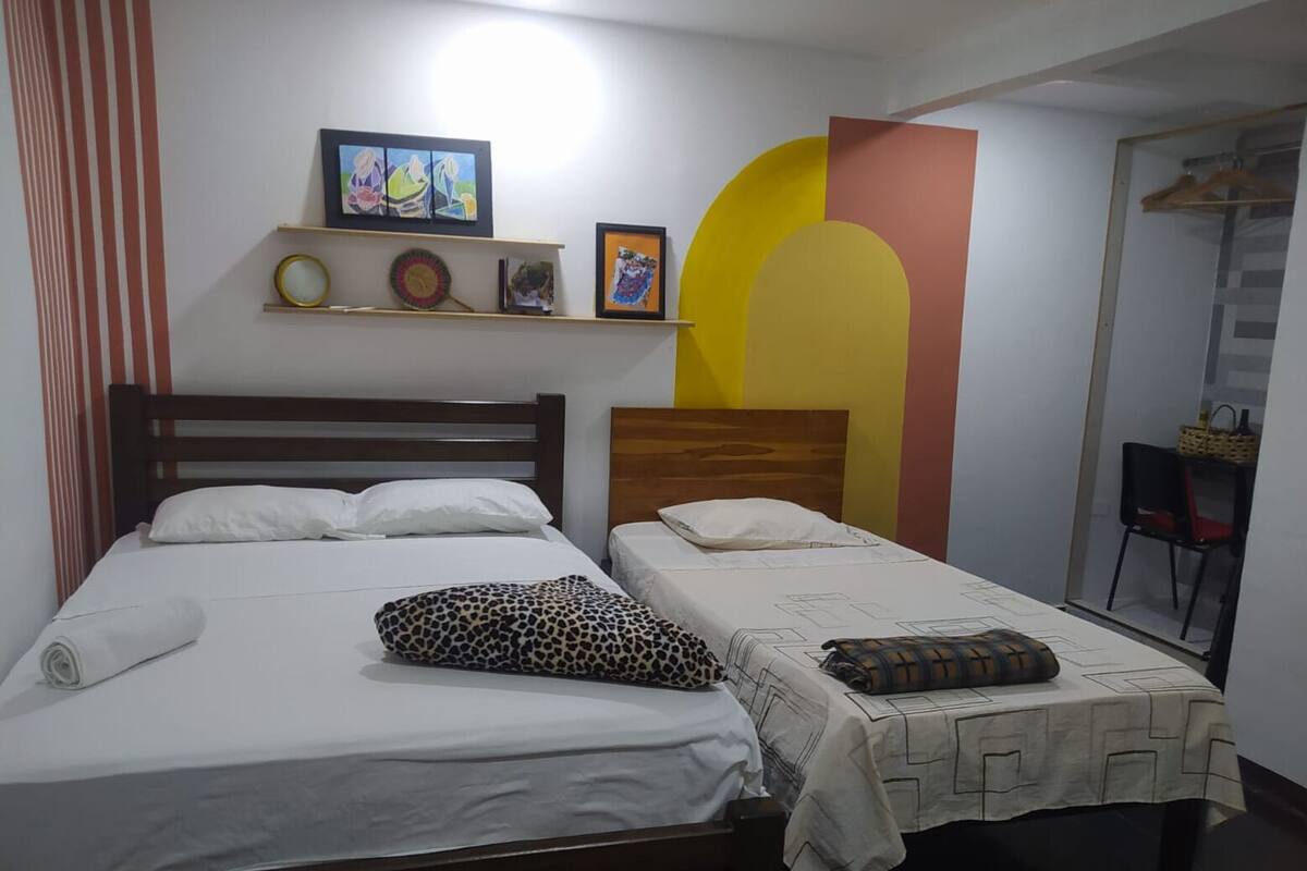 A double bed with white linens and a leopard print pillow, a wooden headboard, and a shelf with framed artwork.