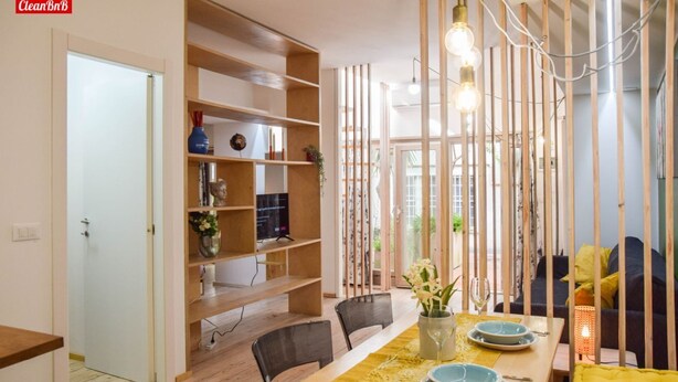 Un comedor con mesa de madera dispuesta para dos personas, una estantería y vista a través de un panel de madera.