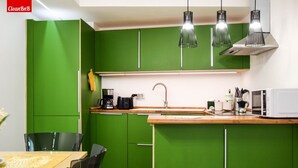 Una cocina con armarios verdes, encimera de madera, pileta, cafetera y luces colgantes.