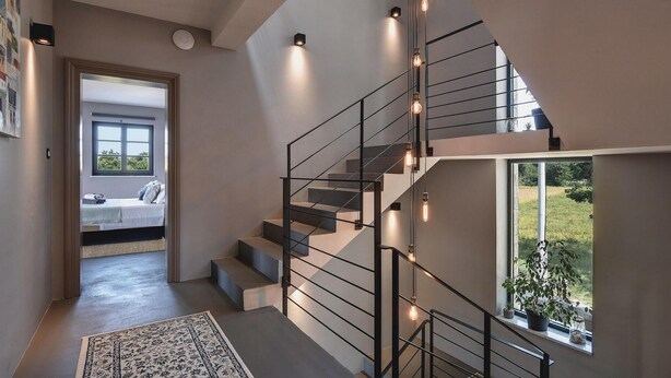 A modern staircase with exposed metal railings and hanging light bulbs, leading to a bedroom with a large window and a view of greenery outside. - Awesome home in Svetvincenat (Svetvincenat)