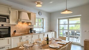A modern kitchen with white cabinetry, a built-in oven, and a dining area set for six with a large window offering a view of the outdoors. - Gorgeous home in Porec (Porec)