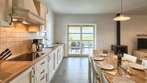 A modern kitchen with a large island, a dining area with a table set for six, and a view through a glass door to an outdoor patio. - Gorgeous home in Porec (Porec)