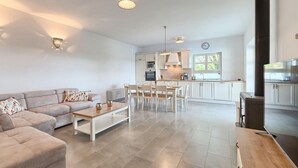 A modern living room with a sofa, coffee table, and dining area. There is a kitchen with white cabinets and a large window. - Gorgeous home in Porec (Porec)