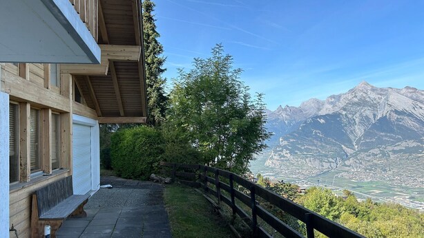 Un balcón de madera con vista a una cordillera y un valle.