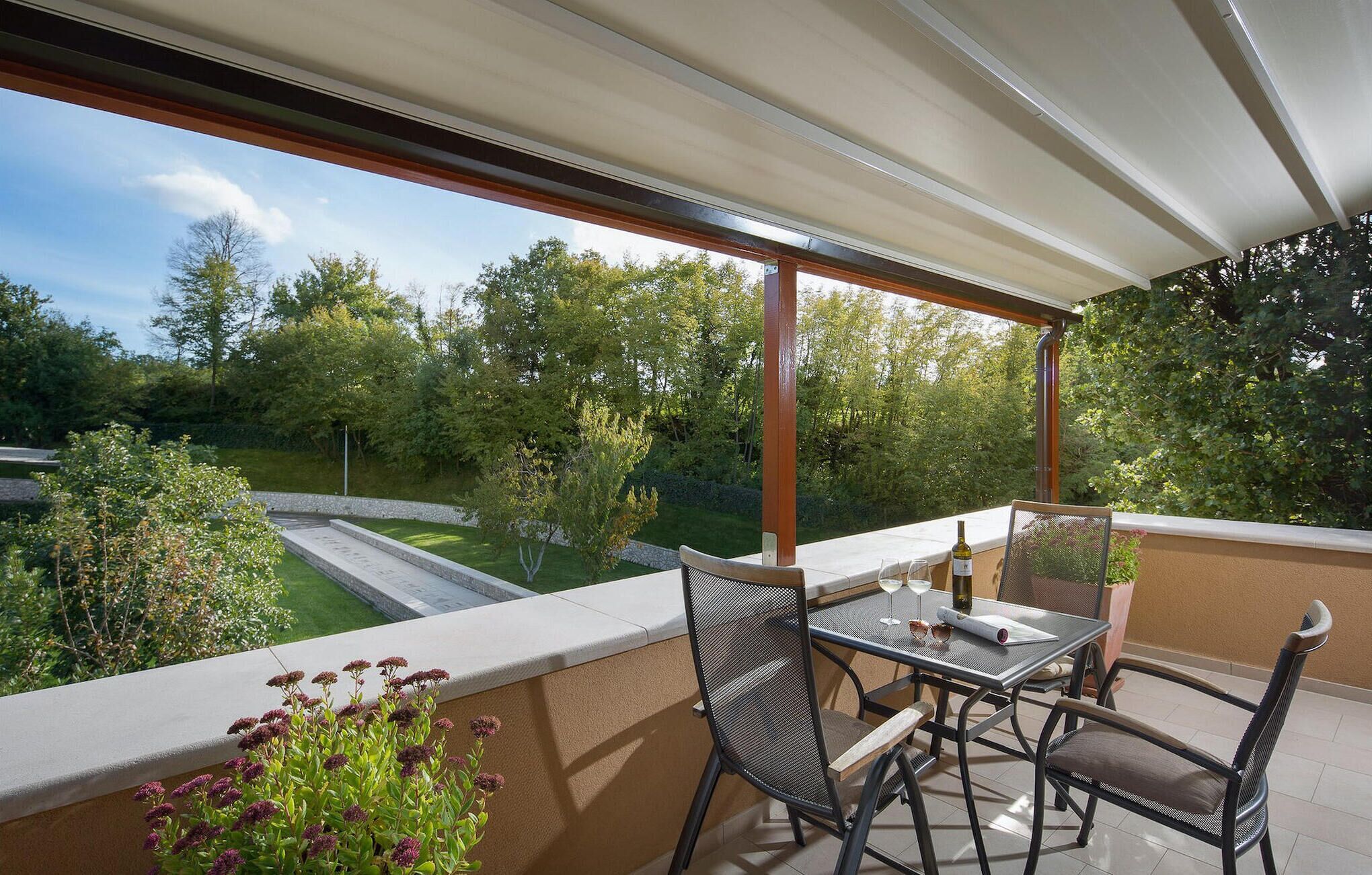 Een balkon met een tafel en stoelen, met uitzicht op een tuin en bomen.
