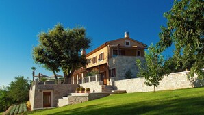 Une maison à deux étages avec des murs en pierre et un grand arbre devant.