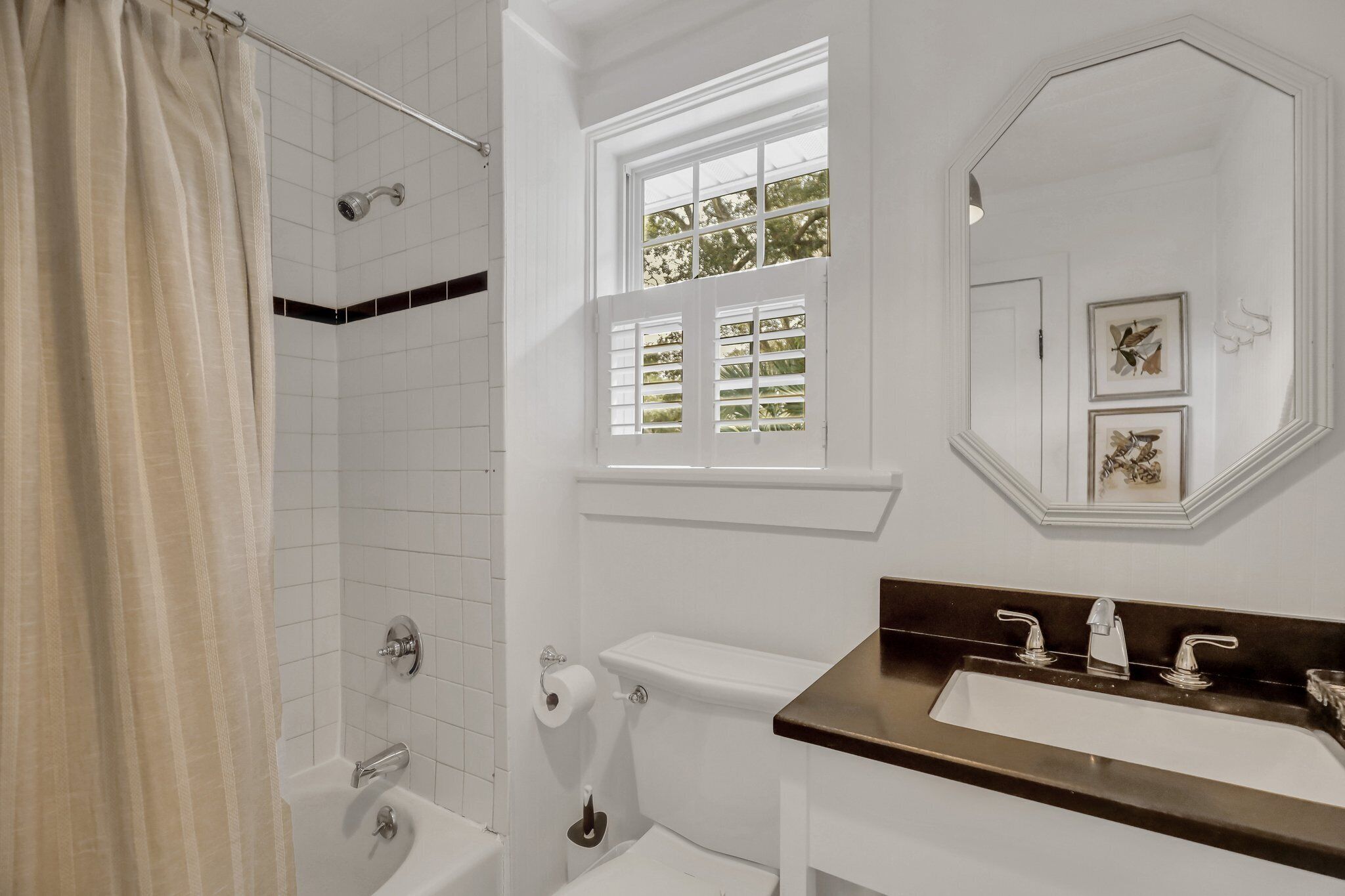 A bathroom with a bathtub, toilet, sink, and window with shutters.