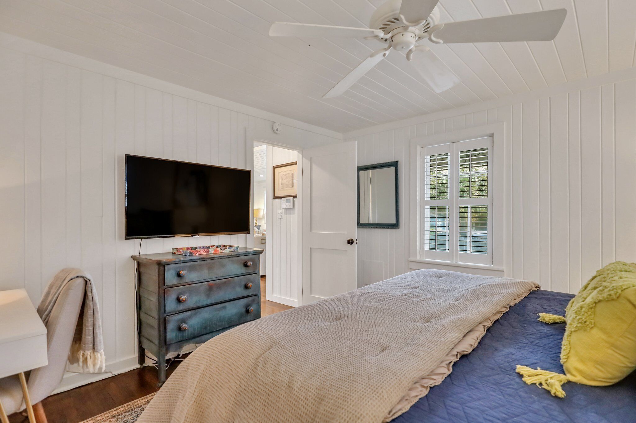 A bedroom with a bed, dresser, television, and a ceiling fan.