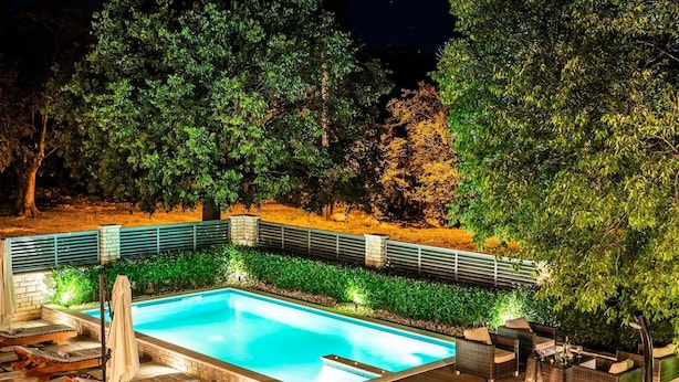 A rectangular swimming pool with a stone border, surrounded by a wooden deck and lounge chairs.