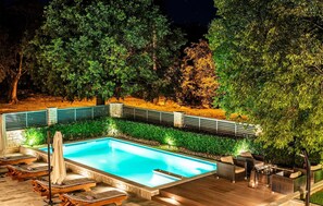 A rectangular swimming pool with a stone border, surrounded by a wooden deck and lounge chairs.