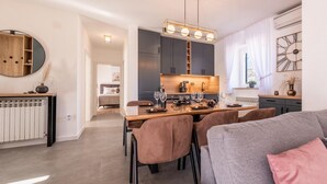 A modern kitchen with a dining area, featuring a central island with chairs, a pendant light, and a view of the adjacent bedroom.