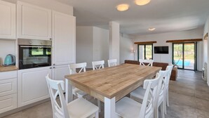 Eine moderne Küche mit weißen Schränken, einem Holztisch und weißen Stühlen.