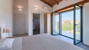 Ein Schlafzimmer mit einem großen Bett, einer Nachttischlampe, einer Schiebeglastür zu einem Balkon und einer Wand-Klimaanlage.