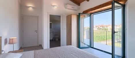 A bedroom with a large bed, a bedside lamp, a sliding glass door to a balcony, and an air conditioning unit on the wall.