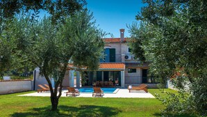 Eine Villa mit Swimmingpool, Sitzgelegenheiten im Freien und einem Garten.