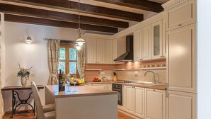 A kitchen with white cabinets, a central island, a stove, and a window with curtains. - Amazing home in Tinjan (Tinjan)