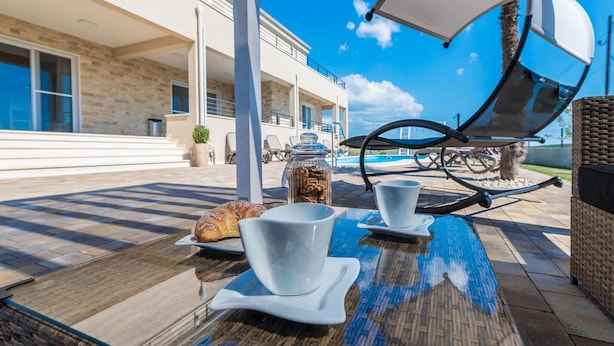 Un espacio exterior para comer con una mesa de vidrio, tazas blancas y un croissant.