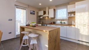 Una cocina moderna con una isla de madera, armarios blancos y un horno empotrado. Hay dos taburetes en la isla y una ventana con cortinas.