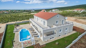 Una casa moderna de dos pisos con piscina, techo de tejas rojas y vistas al paisaje circundante.
