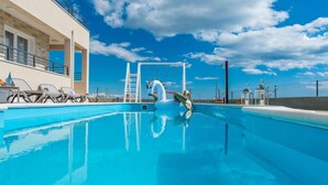 Una piscina con un flotador con forma de cisne, sillas de descanso y vistas al mar bajo un cielo despejado.