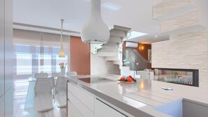 Una cocina moderna con una isla central, iluminación colgante y vistas al salón.