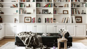 A living room with a bookshelf filled with books and decorative items, a green sofa, and a small table with a vase and a bottle. - Cosy Retreat with Mountain Views (Warburton)