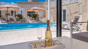 Blick auf ein Schwimmbecken mit einer Flasche Freixenet Champagner, einem Glas und Liegestühlen.