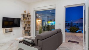 Ein Wohnzimmer mit Flachbildfernseher, grauem Sofa, Bücherregal und Glastür zum Außenbereich.