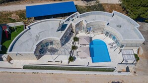 Ein modernes Gebäude mit einem zentralen Schwimmbecken, mehreren Balkonen und einem überdachten Bereich mit einem blauen Dach.