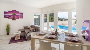Ein modernes Wohnzimmer mit Essbereich, großen Fenstern und Blick auf einen Swimmingpool.