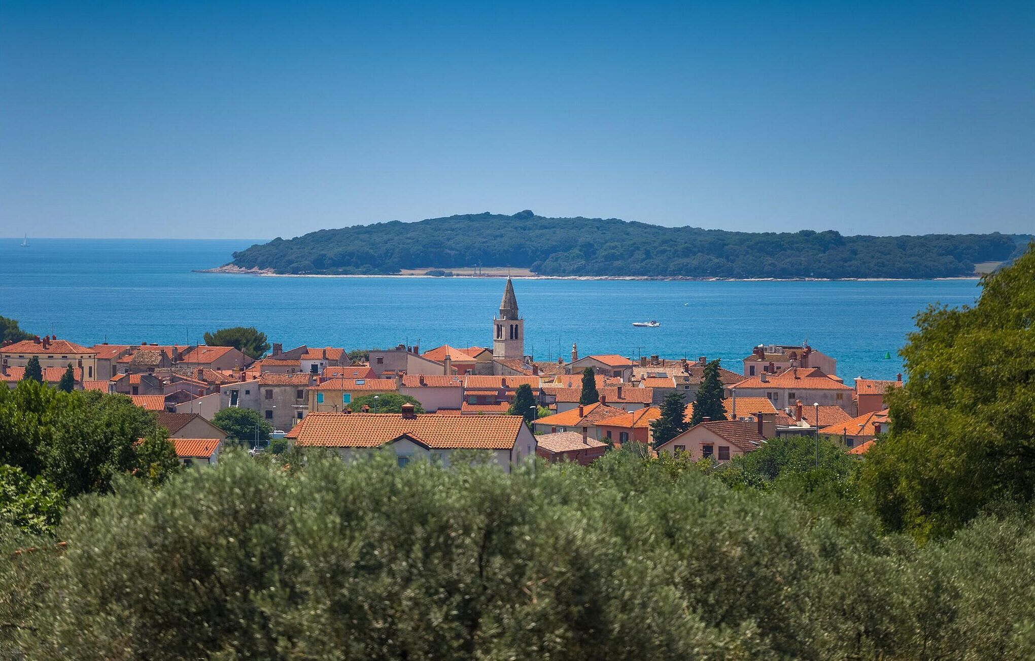A coastal town with red-tiled rooftops, a prominent church tower, and a clear view of the sea.