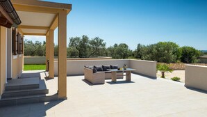 A covered outdoor patio with a sofa and table, steps leading to a building, and a view of trees and hills. - Awesome home in Fazana (Fazana)