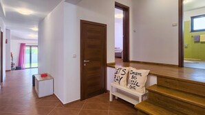 Un pasillo con una puerta de madera, un banco con almohadones y vistas a una habitación con una cama.