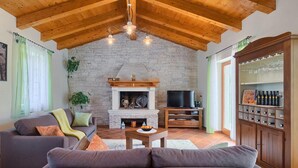 Ein Wohnzimmer mit Kamin aus Stein, Holzbalkendecke, einer Couch, einem Fernseher und einem Weinkühlschrank.