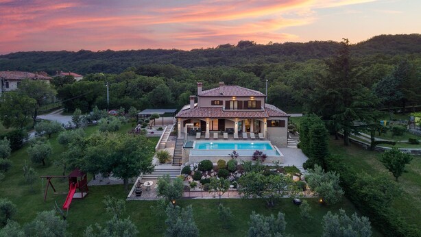 Une maison à deux étages avec une piscine, entourée d’un jardin bien entretenu et d’arbres.