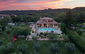 Une maison à deux étages avec une piscine, entourée d’un jardin bien entretenu et d’arbres.