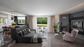 Un salon moderne avec un canapé, un fauteuil rose, une cheminée et un coin repas comprenant une table et des chaises.