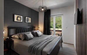 Une chambre moderne avec un grand lit, une table de chevet, une commode, un luminaire suspendu et un téléviseur fixé au mur.