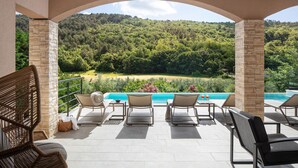Une terrasse avec une piscine, des piliers en pierre et une vue sur une colline boisée.