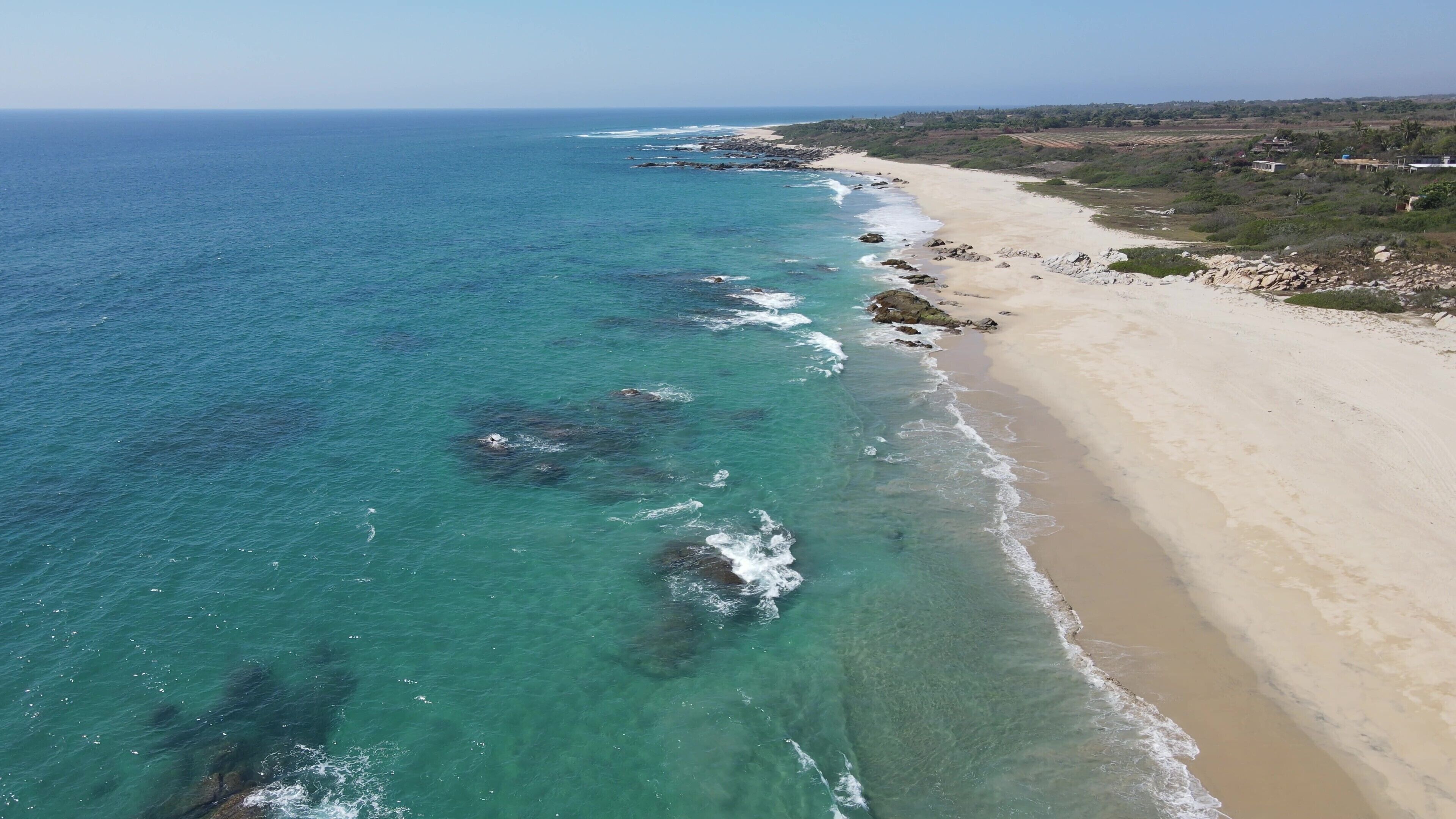 Een luchtbeeld van een strand met helder turquoise water, een zandstrand en verspreide rotsen.