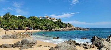 Una playa con costa rocosa, agua azul cristalina y edificios en una colina.
