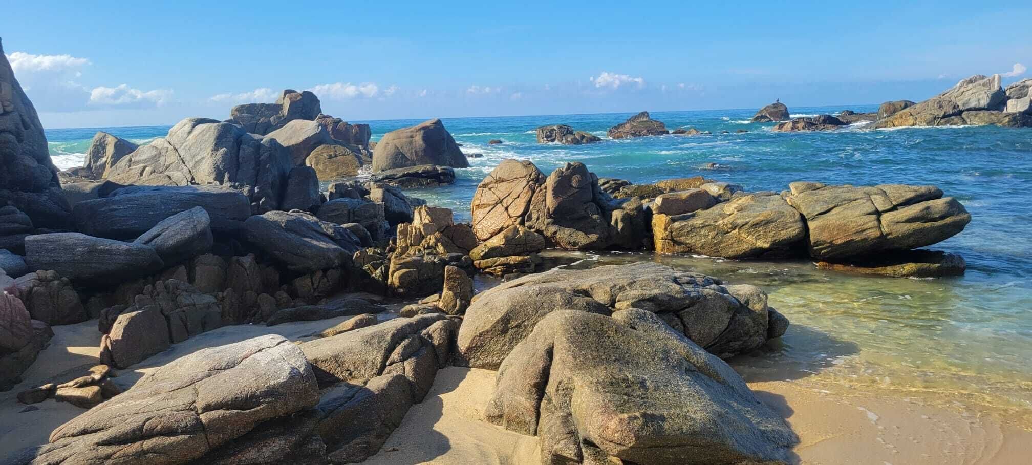A rocky beach with large boulders and clear blue water.