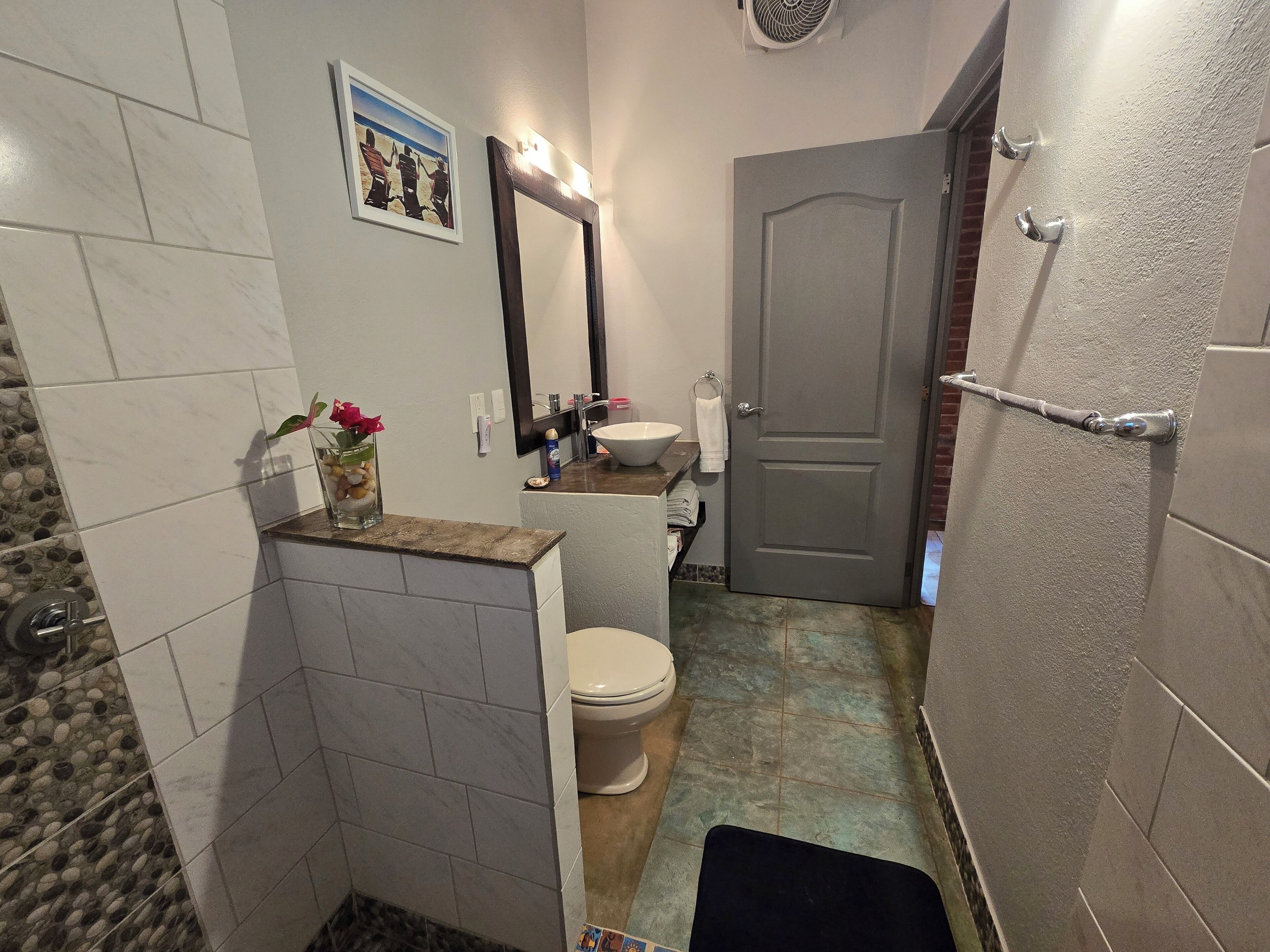 Une salle de bain avec des toilettes, un lavabo et un miroir. Une porte donne accès à une autre pièce.
