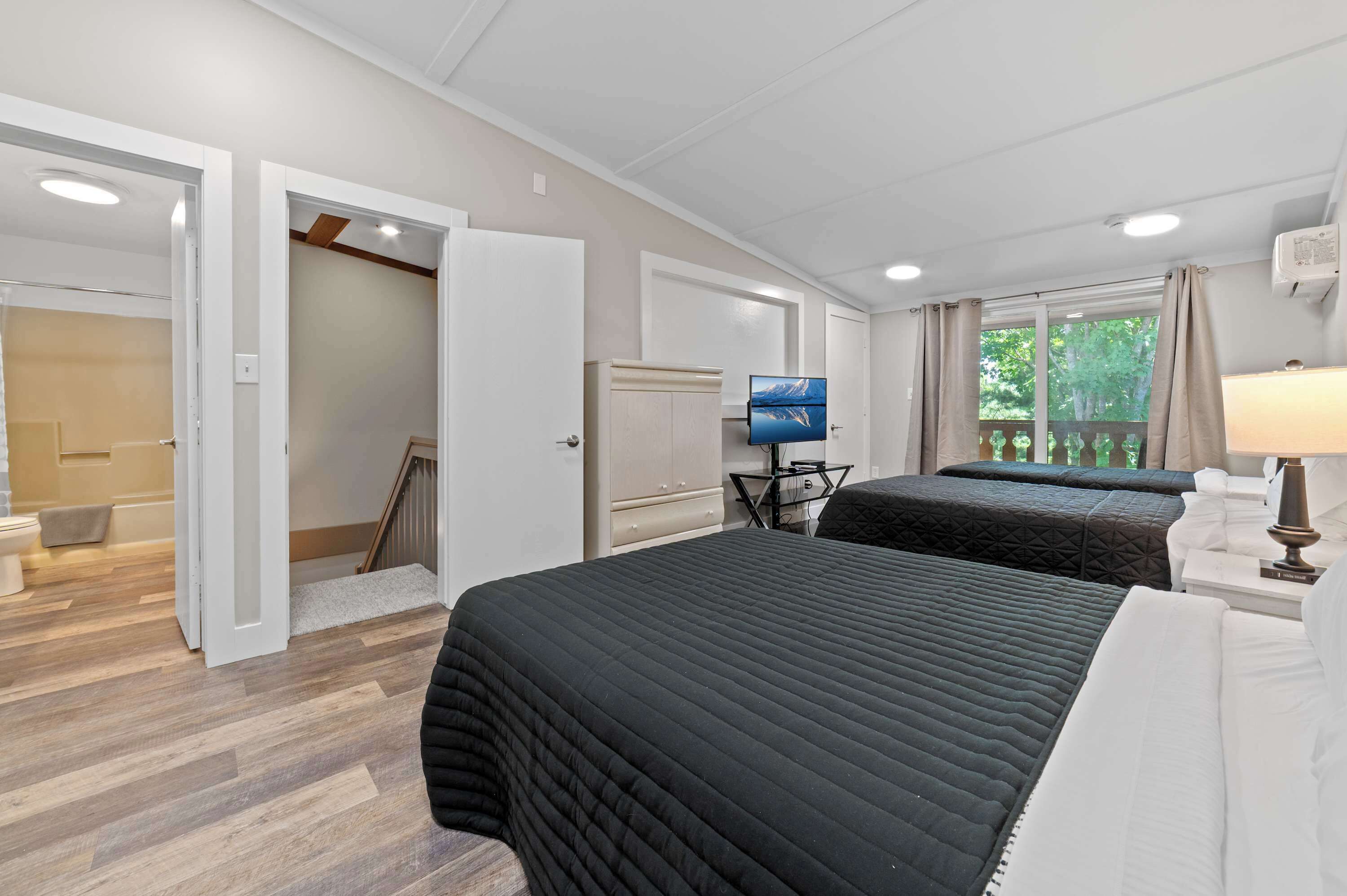 A hotel room with two beds, a television, a desk with a lamp, and a window with curtains.