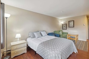 A bedroom with a bed, bedside table, lamp, and a small wooden side table with a book. - Schuss Mountain Ski/Golf Condo (Mancelona)