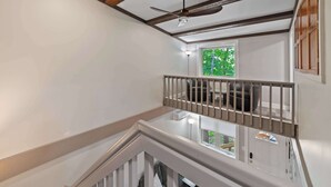 Una habitación con ventilador de techo, ventana con vista a la vegetación y escalera con barandilla.