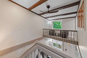 Una habitación con ventilador de techo, ventana con vista a la vegetación y escalera con barandilla.
