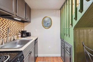 A compact kitchen with a checkered backsplash, a coffee maker, and a framed picture on the wall. - Schuss Mountain Ski/Golf Condo (Mancelona)